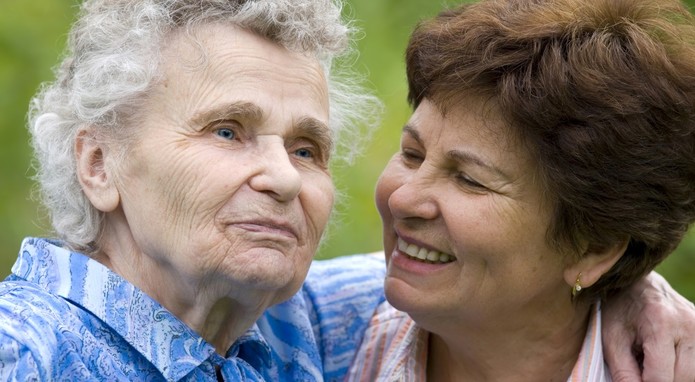 Eine schon etwas ältere Frau schaut lächelnd in das Gesicht einer Seniorin, die ihre Mutter sein könnte.